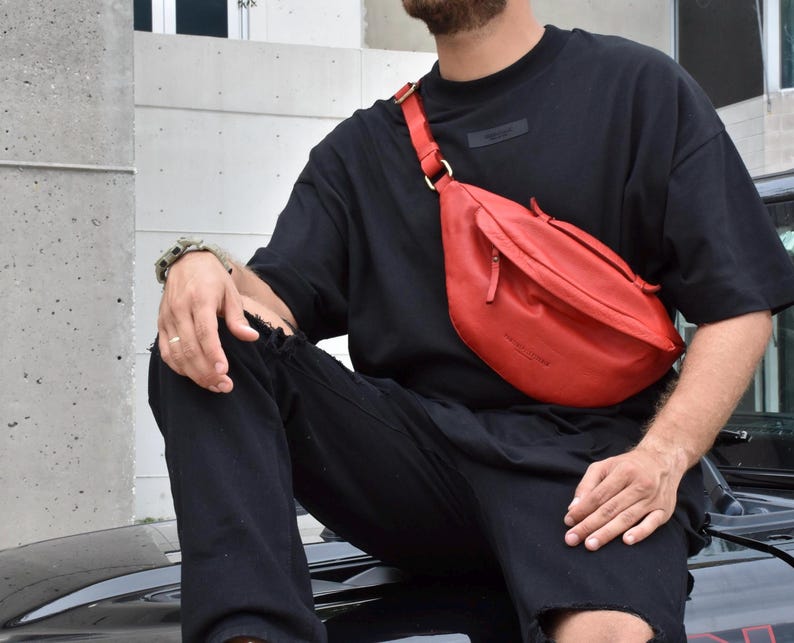 Man wearing a red leather fanny pack over a black outfit. This stylish crossbody bag is a perfect blend of trend and functionality, ideal for everyday use or festivals. A modern, high-quality leather bag for carrying essentials