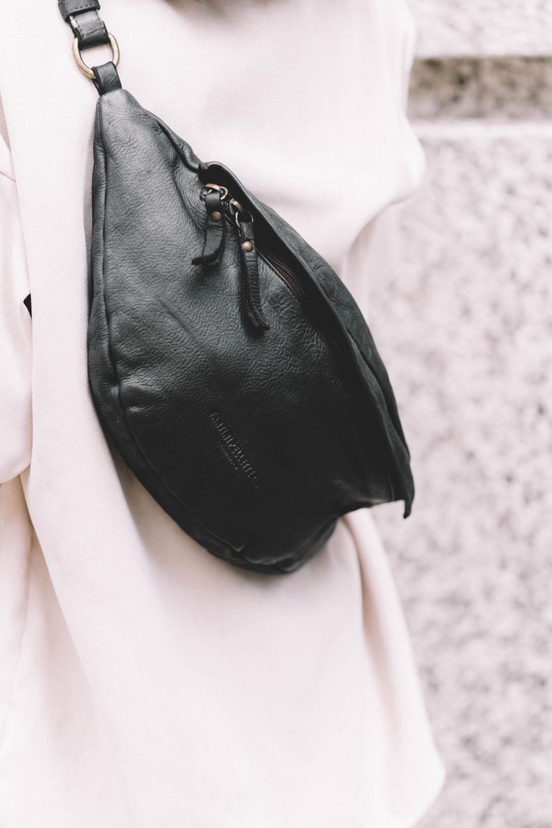 Black leather hip bag draped over a white outfit. This modern waist bag offers a sleek, minimalist look suitable for any outfit. A luxurious yet practical leather travel bag for those who value both style and convenience