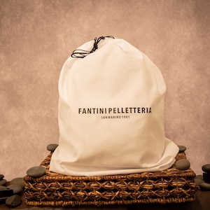 A cream-colored dust bag with “Fantini Pelletteria” branding, placed on an ornate surface, highlighting luxury packaging for premium leather goods.