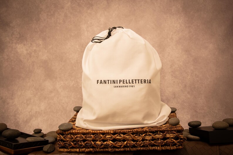 A cream-colored dust bag with “Fantini Pelletteria” branding, placed on an ornate surface, highlighting luxury packaging for premium leather goods.