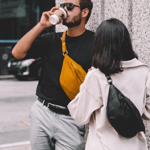 Man drinking coffee while wearing a mustard-yellow leather side bag crossbody. The casual and vibrant color choice makes this bag a unique fashion accessory.
