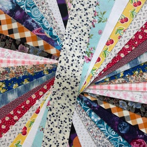 Może przedstawiać: Wachlarz zróżnicowanych pasków materiału o różnych wzorach i kolorach. Wzory obejmują motywy kwiatowe, kratę i abstrakcyjne w odcieniach niebieskiego, czerwonego, żółtego i białego. Paski materiału ułożone są w układzie radialnym.