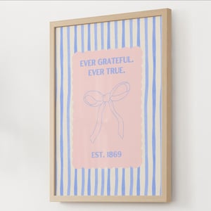 May include: A framed print with a light wood frame. The print features a pink rectangle with a bow illustration and the text "EVER GRATEFUL. EVER TRUE. EST. 1869." The background has blue and white vertical stripes.