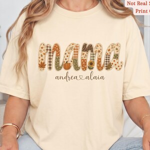 Personalized Mama Comfort Colors shirt with custom kids names, fall patchwork letters, pumpkins, florals, and faux embroidery effect in warm autumn tones on an ivory tee.