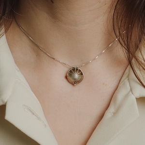 Peut inclure: Un collier en argent avec un pendentif rond orné d'un motif soleil. Le pendentif est suspendu à une chaîne délicate.