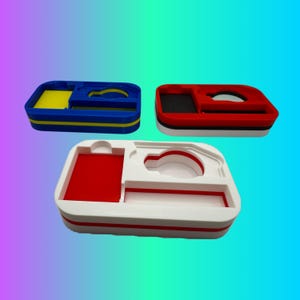 May include: Three 3D printed organizers with different colored compartments. The first organizer is blue with yellow compartments, the second is red with black compartments, and the third is white with red compartments.