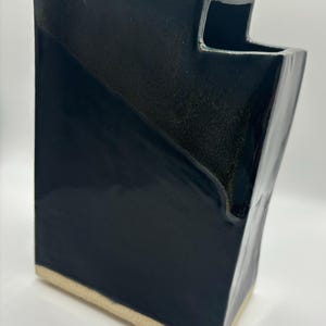 May include: A dark blue ceramic vase with a unique, angular design. The vase has a white rim and a textured surface.