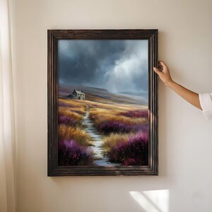 May include: A framed landscape painting depicts a path leading to a small house on a hill under a dramatic, cloudy sky. The artwork features vibrant colors of purple, gold, and green, with a dark brown wooden frame.