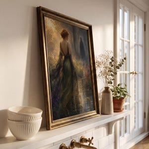 May include: A framed art print depicts a woman in a flowing green gown walking through a sunlit forest. The artwork has a gold-colored frame and is displayed on a white shelf. A vase with dried flowers and a potted plant are also on the shelf.
