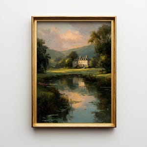 May include: A framed landscape painting depicts a serene scene with a large white house nestled among green trees and rolling hills. A calm body of water reflects the sky and surrounding scenery. The painting is in a gold frame.