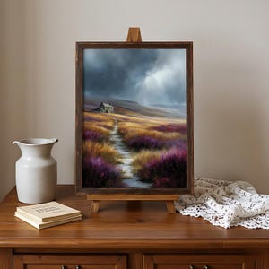 May include: A framed landscape painting on a wooden easel depicts a path leading to a small house under a stormy sky. The path winds through fields of purple and gold flowers. A white vase and a stack of books sit nearby.