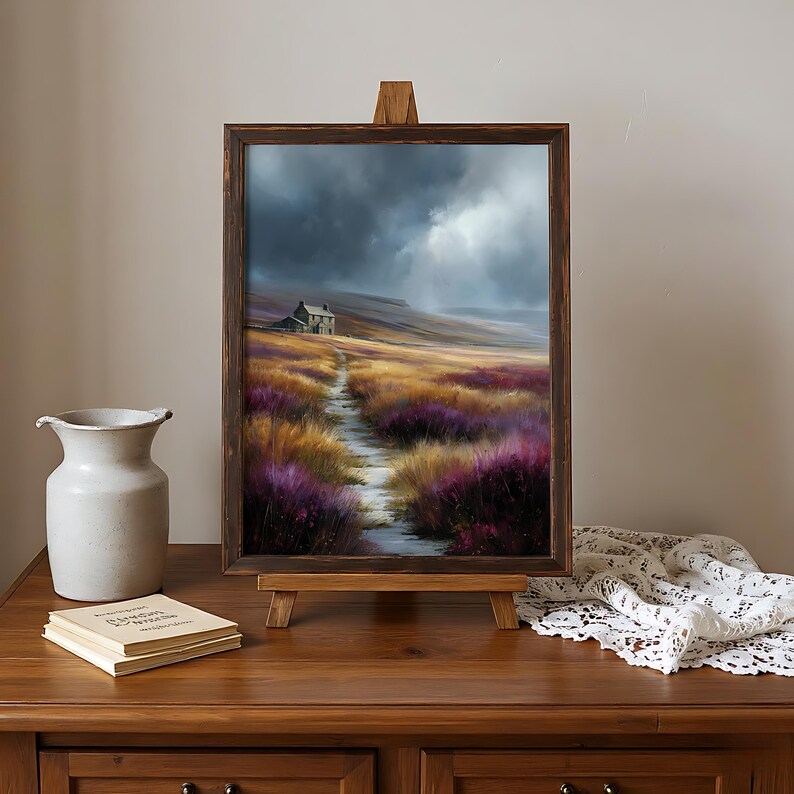 May include: A framed landscape painting on a wooden easel depicts a path leading to a small house under a stormy sky. The path winds through fields of purple and gold flowers. A white vase and a stack of books sit nearby.