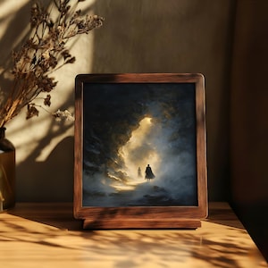 May include: A framed art print depicts two figures walking towards a bright light within a dark, cavernous landscape. The wooden frame has a warm, natural finish. A vase with dried flowers sits to the left, casting shadows on the wooden surface.