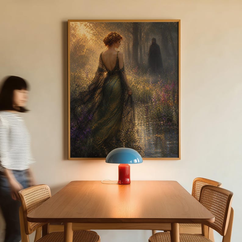 May include: A framed painting depicts a woman in a flowing gown in a forest scene. A blue and red table lamp sits on a wooden table. Two wicker chairs are positioned near the table. A person is walking past the table.