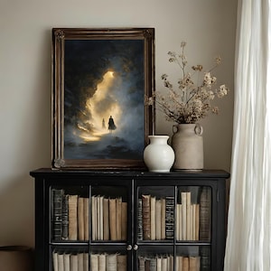 May include: A framed painting with a dark, dramatic landscape featuring two figures walking towards a bright light. The painting is displayed on a black cabinet with glass doors, filled with books. A white vase and a rustic vase with dried flowers are also on the cabinet.