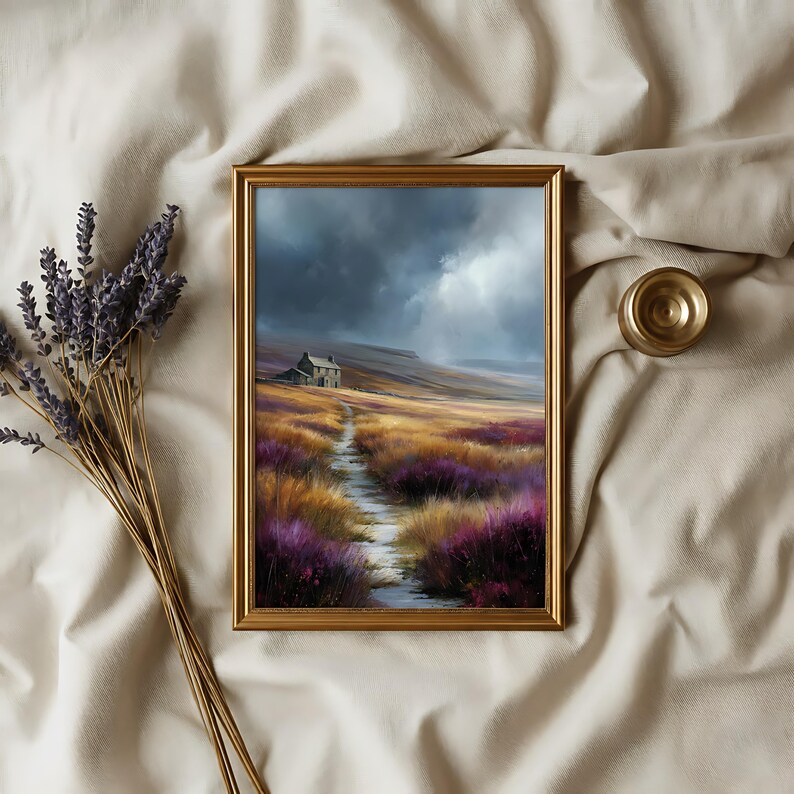 May include: A framed landscape painting depicts a path leading to a small house under a stormy sky. The path winds through fields of purple and gold flowers. A bundle of lavender and a small gold-colored object are next to the frame.