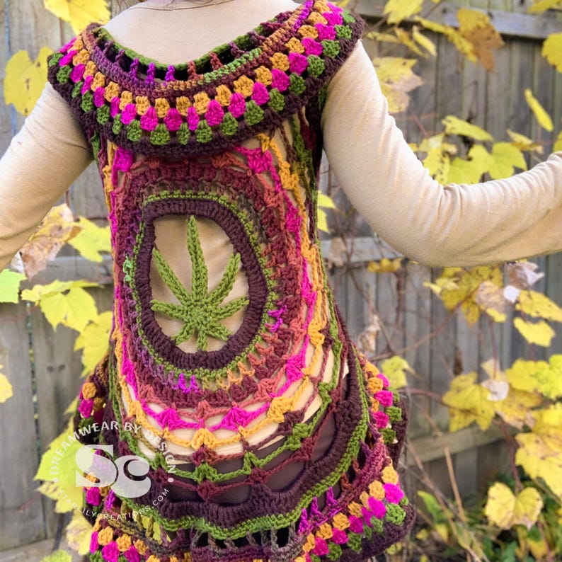 May include: A crocheted vest with a colorful mandala design featuring a green marijuana leaf in the center. The vest is made with a variety of shades of brown, pink, green, and yellow yarn.