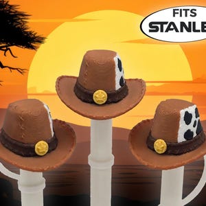 May include: Three brown cowboy hats with white and black cow print accents on the side, a dark brown band, and a gold-colored circular emblem on the front. The text FITS STANLEY is displayed in an oval at the top right of the image.