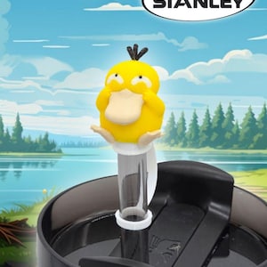 May include: A yellow character-themed Stanley cup topper with a cartoon duck design. The topper is attached to a clear straw and sits atop a black and white Stanley cup. The text "FITS STANLEY" is in a white oval.