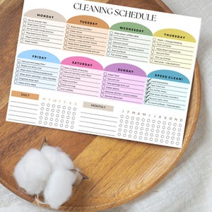 May include: A colorful cleaning schedule notepad with sections for each day of the week, including tasks like vacuuming, wiping surfaces, and laundry. The notepad has a daily and monthly checklist.