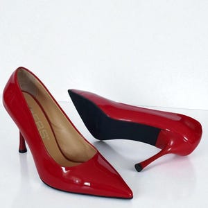 May include: A pair of glossy red high heels with pointed toes and stiletto heels. The shoes are patent leather and have a sleek, elegant design. The heels are approximately 7.6 cm tall.