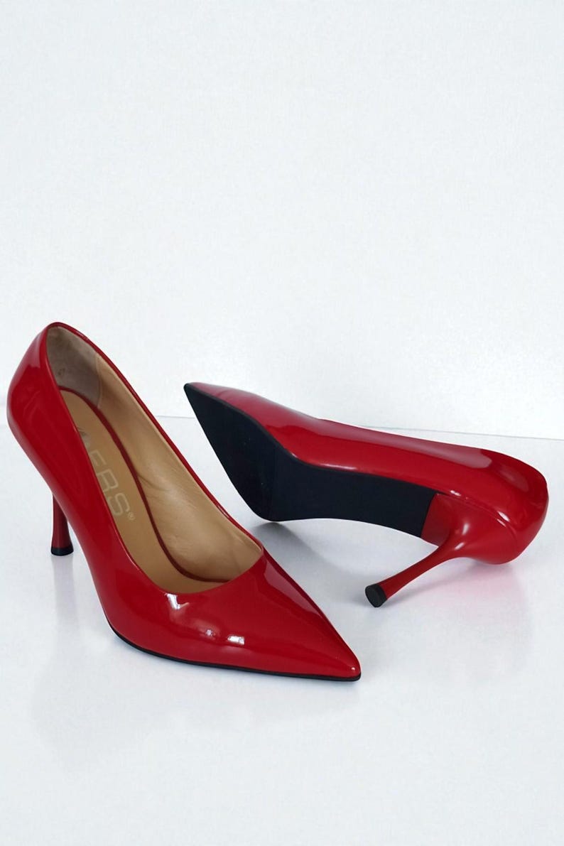 May include: A pair of glossy red high heels with pointed toes and stiletto heels. The shoes are patent leather and have a sleek, elegant design. The heels are approximately 7.6 cm tall.