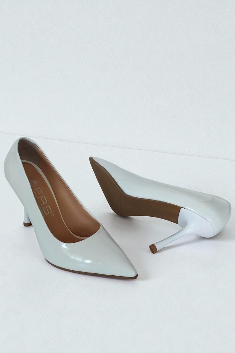 May include: A pair of pale blue high-heeled shoes with pointed toes. The heels are thin and the soles are brown. The shoes have a glossy finish and are set against a white background. The brand name is visible on the insole.