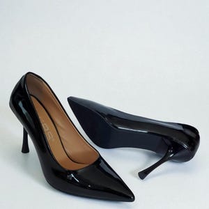 May include: A pair of glossy black high-heeled shoes with pointed toes. The heels are slender and stiletto-style. The shoes are set against a white background, highlighting their sleek design.