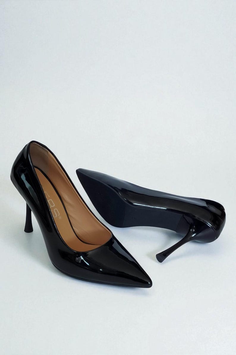 May include: A pair of glossy black high-heeled shoes with pointed toes. The heels are slender and stiletto-style. The shoes are set against a white background, highlighting their sleek design.