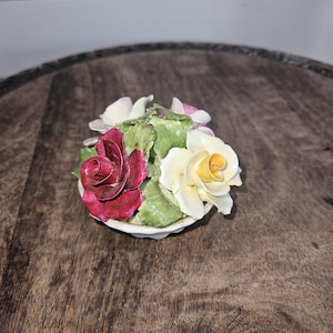 May include: A porcelain figurine of a bouquet of flowers in a white pot. The flowers are red, yellow, and pink.