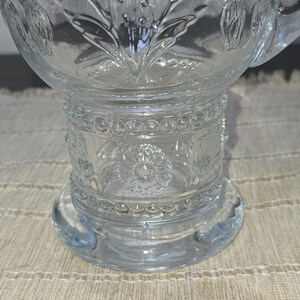 May include: Clear glass punch bowl with intricate floral and geometric patterns. The bowl features a wide base, a detailed midsection, and a decorative rim. The glass is transparent, allowing light to pass through, and is ideal for serving beverages at gatherings.