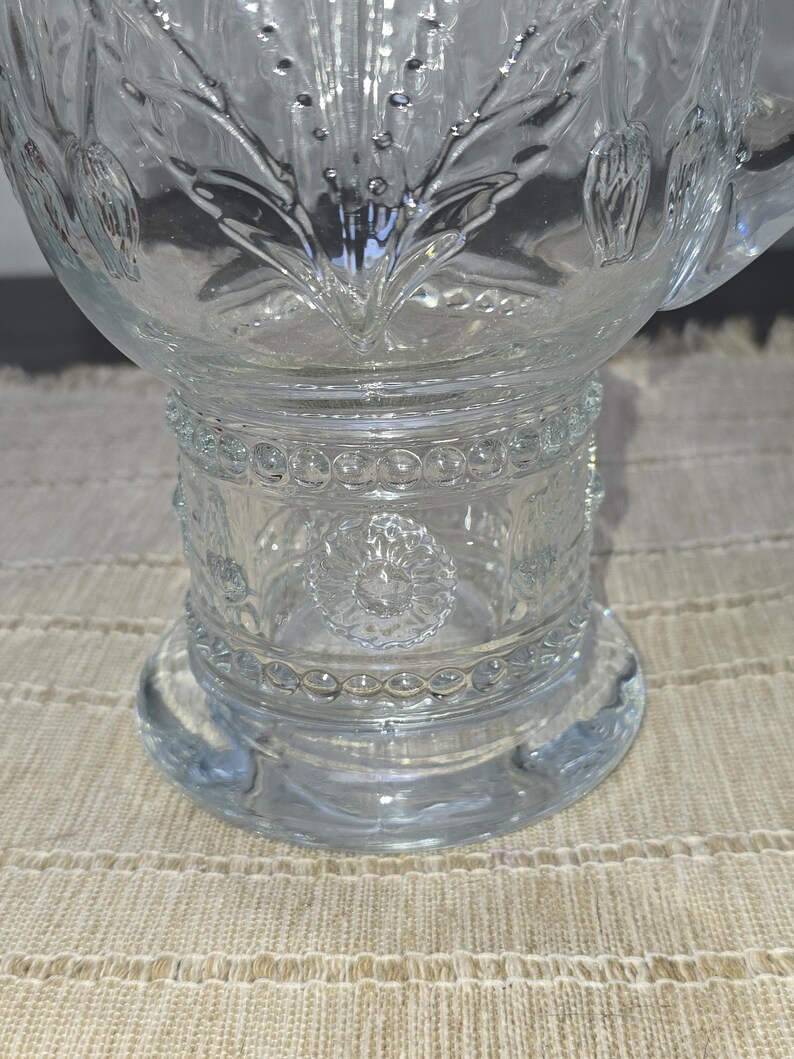May include: Clear glass punch bowl with intricate floral and geometric patterns. The bowl features a wide base, a detailed midsection, and a decorative rim. The glass is transparent, allowing light to pass through, and is ideal for serving beverages at gatherings.
