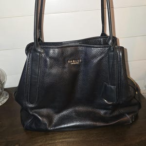 May include: Black leather tote bag with gold hardware and the Radley London logo.