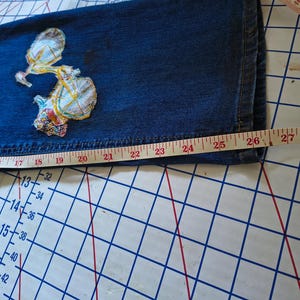 Patchwork Boho AppliquePatched Upcycled Cropped DarkerDenim Cuffed or Straight Jeans SIZE 14 TO 16 Stretch VintageStyledenim.   Inseam 26.  Vintage-look handpainted throughout Flowers, Birds, Cat, and appliques of various designs.  Handmade and handcrafted.   Unique Applique Jeans Distressed.  Highrise High Waisted, Handpainted Handmade Appliqued Straight Style Jeans. Size 14 to 16 depending on your measurements.  Check the measurements.  Handmade Boho Sash Bohemian design crocheted with bells.