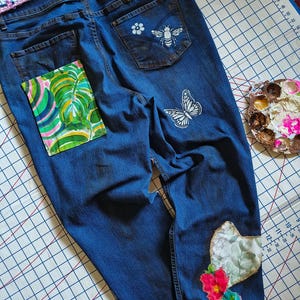 Patchwork Boho AppliquePatched Upcycled Cropped DarkerDenim Cuffed or Straight Jeans SIZE 14 TO 16 Stretch VintageStyledenim.   Inseam 26.  Vintage-look handpainted throughout Flowers, Birds, Cat, and appliques of various designs.  Handmade and handcrafted.   Unique Applique Jeans Distressed.  Highrise High Waisted, Handpainted Handmade Appliqued Straight Style Jeans. Size 14 to 16 depending on your measurements.  Check the measurements.  Handmade Boho Sash Bohemian design crocheted with bells.