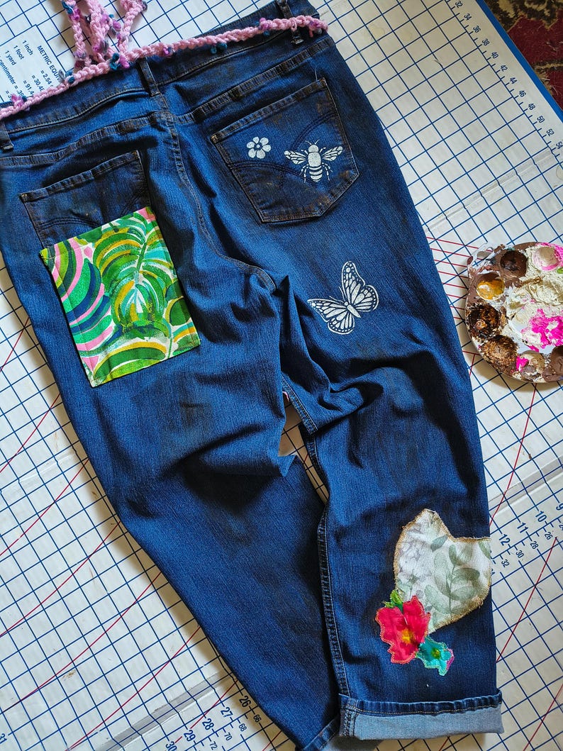 Patchwork Boho AppliquePatched Upcycled Cropped DarkerDenim Cuffed or Straight Jeans SIZE 14 TO 16 Stretch VintageStyledenim.   Inseam 26.  Vintage-look handpainted throughout Flowers, Birds, Cat, and appliques of various designs.  Handmade and handcrafted.   Unique Applique Jeans Distressed.  Highrise High Waisted, Handpainted Handmade Appliqued Straight Style Jeans. Size 14 to 16 depending on your measurements.  Check the measurements.  Handmade Boho Sash Bohemian design crocheted with bells.