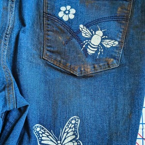 Patchwork Boho AppliquePatched Upcycled Cropped DarkerDenim Cuffed or Straight Jeans SIZE 14 TO 16 Stretch VintageStyledenim.   Inseam 26.  Vintage-look handpainted throughout Flowers, Birds, Cat, and appliques of various designs.  Handmade and handcrafted.   Unique Applique Jeans Distressed.  Highrise High Waisted, Handpainted Handmade Appliqued Straight Style Jeans. Size 14 to 16 depending on your measurements.  Check the measurements.  Handmade Boho Sash Bohemian design crocheted with bells.