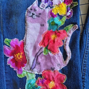 Patchwork Boho AppliquePatched Upcycled Cropped DarkerDenim Cuffed or Straight Jeans SIZE 14 TO 16 Stretch VintageStyledenim.   Inseam 26.  Vintage-look handpainted throughout Flowers, Birds, Cat, and appliques of various designs.  Handmade and handcrafted.   Unique Applique Jeans Distressed.  Highrise High Waisted, Handpainted Handmade Appliqued Straight Style Jeans. Size 14 to 16 depending on your measurements.  Check the measurements.  Handmade Boho Sash Bohemian design crocheted with bells.