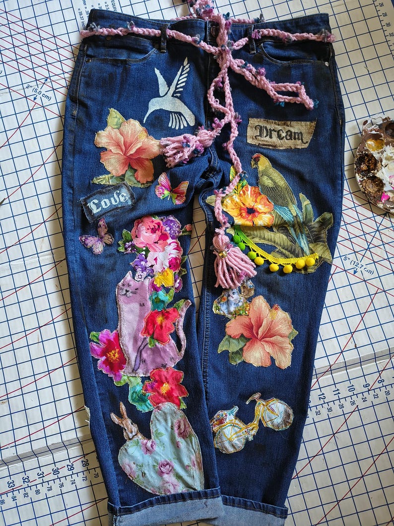 Patchwork Boho AppliquePatched Upcycled Cropped DarkerDenim Cuffed or Straight Jeans SIZE 14 TO 16 Stretch VintageStyledenim.   Inseam 26.  Vintage-look handpainted throughout Flowers, Birds, Cat, and appliques of various designs.  Handmade and handcrafted.   Unique Applique Jeans Distressed.  Highrise High Waisted, Handpainted Handmade Appliqued Straight Style Jeans. Size 14 to 16 depending on your measurements.  Check the measurements.  Handmade Boho Sash Bohemian design crocheted with bells.