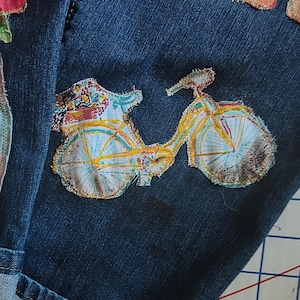 Patchwork Boho AppliquePatched Upcycled Cropped DarkerDenim Cuffed or Straight Jeans SIZE 14 TO 16 Stretch VintageStyledenim.   Inseam 26.  Vintage-look handpainted throughout Flowers, Birds, Cat, and appliques of various designs.  Handmade and handcrafted.   Unique Applique Jeans Distressed.  Highrise High Waisted, Handpainted Handmade Appliqued Straight Style Jeans. Size 14 to 16 depending on your measurements.  Check the measurements.  Handmade Boho Sash Bohemian design crocheted with bells.