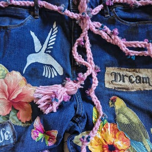 Patchwork Boho AppliquePatched Upcycled Cropped DarkerDenim Cuffed or Straight Jeans SIZE 14 TO 16 Stretch VintageStyledenim.   Inseam 26.  Vintage-look handpainted throughout Flowers, Birds, Cat, and appliques of various designs.  Handmade and handcrafted.   Unique Applique Jeans Distressed.  Highrise High Waisted, Handpainted Handmade Appliqued Straight Style Jeans. Size 14 to 16 depending on your measurements.  Check the measurements.  Handmade Boho Sash Bohemian design crocheted with bells.