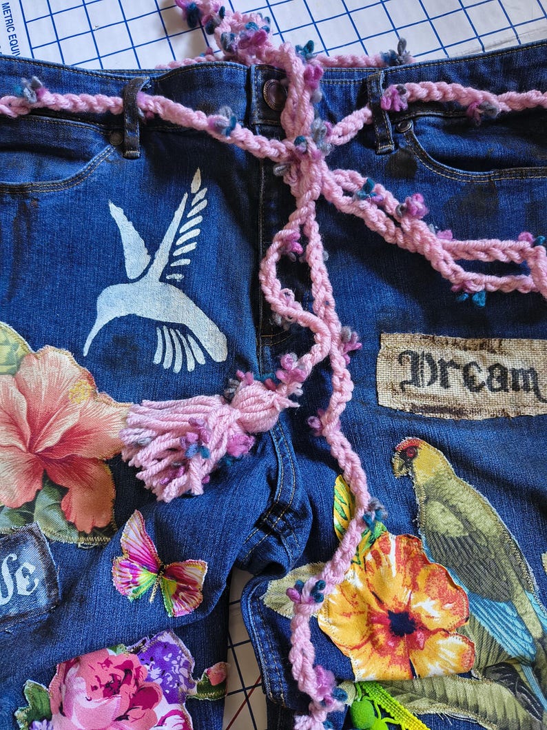 Patchwork Boho AppliquePatched Upcycled Cropped DarkerDenim Cuffed or Straight Jeans SIZE 14 TO 16 Stretch VintageStyledenim.   Inseam 26.  Vintage-look handpainted throughout Flowers, Birds, Cat, and appliques of various designs.  Handmade and handcrafted.   Unique Applique Jeans Distressed.  Highrise High Waisted, Handpainted Handmade Appliqued Straight Style Jeans. Size 14 to 16 depending on your measurements.  Check the measurements.  Handmade Boho Sash Bohemian design crocheted with bells.