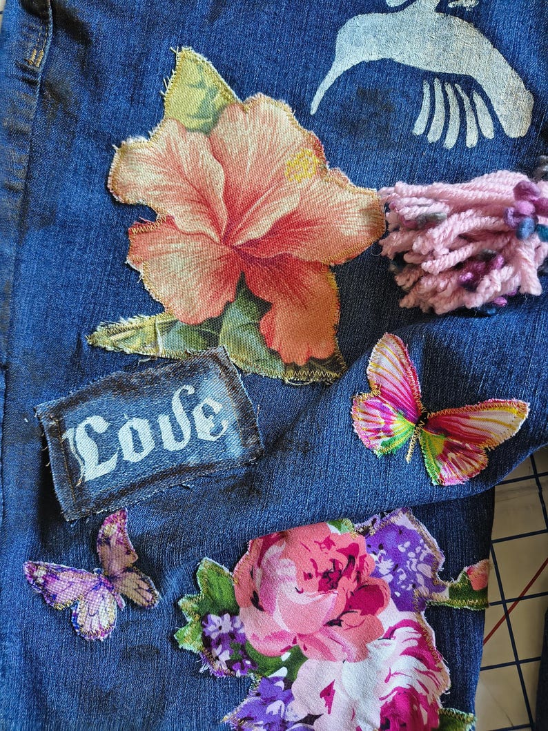 Patchwork Boho AppliquePatched Upcycled Cropped DarkerDenim Cuffed or Straight Jeans SIZE 14 TO 16 Stretch VintageStyledenim.   Inseam 26.  Vintage-look handpainted throughout Flowers, Birds, Cat, and appliques of various designs.  Handmade and handcrafted.   Unique Applique Jeans Distressed.  Highrise High Waisted, Handpainted Handmade Appliqued Straight Style Jeans. Size 14 to 16 depending on your measurements.  Check the measurements.  Handmade Boho Sash Bohemian design crocheted with bells.