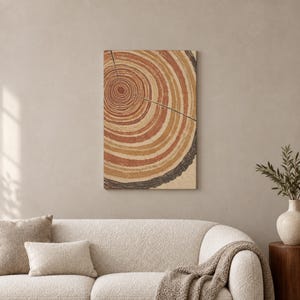 Puede incluir: Una impresión de arte mural rectangular que presenta una sección transversal estilizada de un tronco de árbol. El diseño muestra anillos concéntricos en tonos terracota, naranja quemado y crema, con un borde de corteza texturizado.