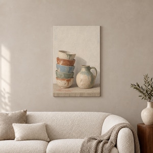May include: A stack of five ceramic bowls in varying colours including cream, terracotta, blue, and sage green, positioned next to a matching ceramic pitcher with a handle. The pottery features a speckled, textured finish and earthy tones.