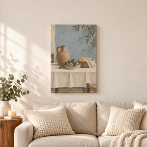 May include: A wall art print depicting a still life scene on a table covered with a white cloth. A tan ceramic pitcher, a bowl filled with dark purple figs, and a woven basket containing bread are arranged against a textured blue wall.