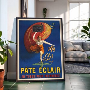 May include: Framed vintage poster with a blue background. The artwork depicts a woman in an orange dress holding a small oven and tubes of product, with the text "PÂTE ÉCLAIR" in yellow. The background features a red and orange swirl.