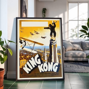 May include: Framed vintage movie poster for "King Kong." The artwork features a large gorilla atop a skyscraper, with biplanes flying in a yellow sky above a cityscape. The title "King Kong" is prominently displayed in white letters.