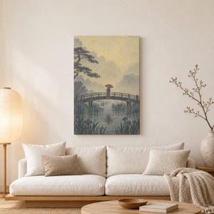 May include: A rectangular wall art print featuring a landscape illustration of a person holding a red umbrella while standing on a wooden arched bridge over a calm river, surrounded by dark blue foliage and trees against a pale yellow sky.