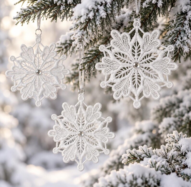 May include: Three white lace snowflake ornaments hanging from a pine tree. Each ornament features intricate threadwork patterns and a small, clear, circular crystal bead at the center. The snowflakes are suspended by thin white ribbons.